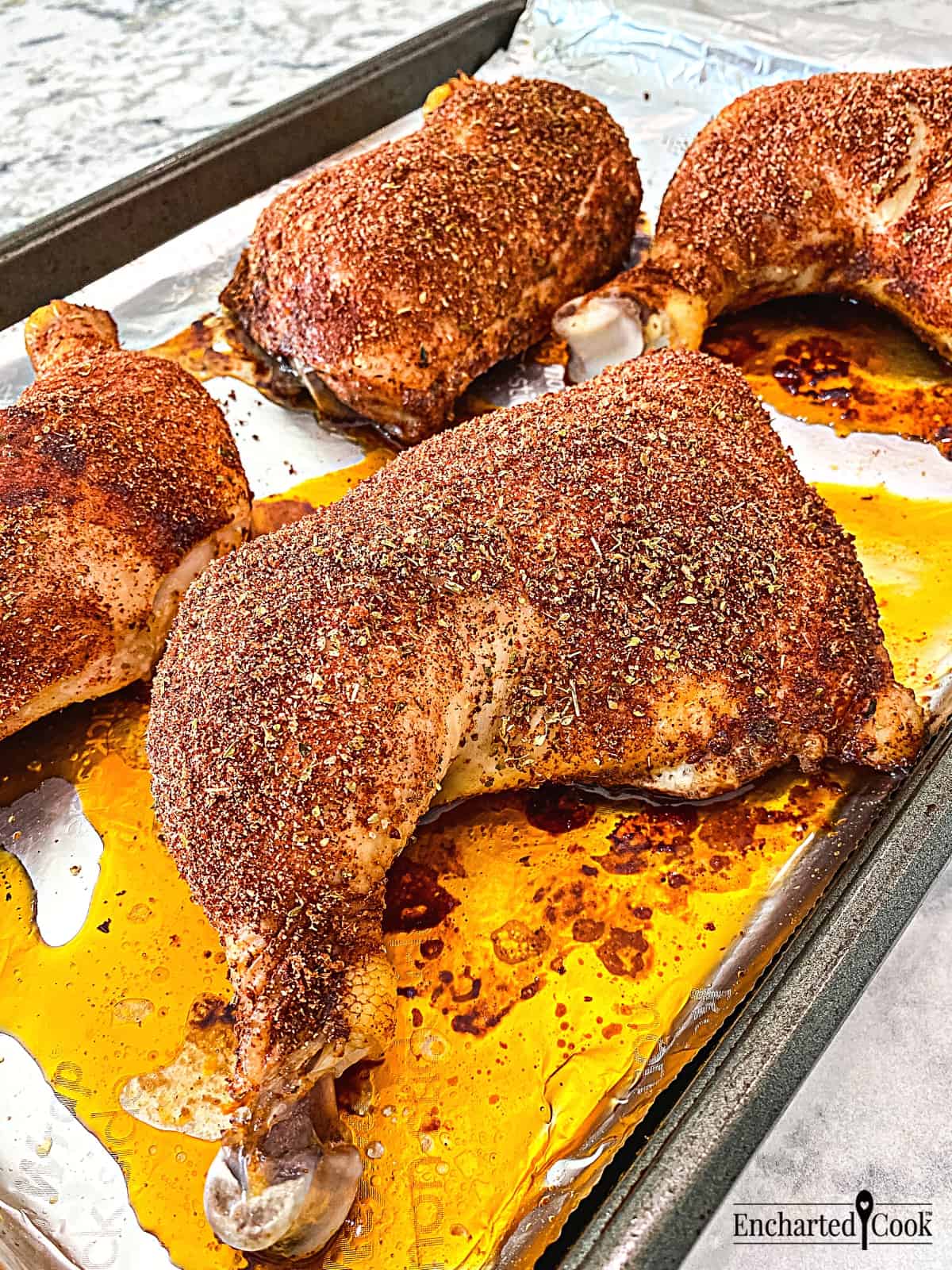 Baked chicken leg quarters coated with in a savory spice rub on a rimmed baking pan.