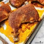 Baked chicken leg quarters coated with in a savory spice rub on a rimmed baking pan.