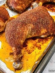 Baked chicken leg quarters coated with in a savory spice rub on a rimmed baking pan.
