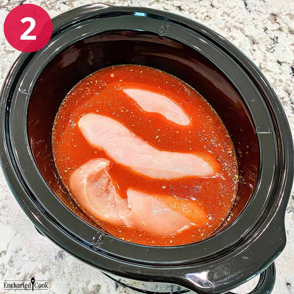 Process Photo 2 - Raw chicken breasts are submerged into the red enchilada sauce in a large crock pot.