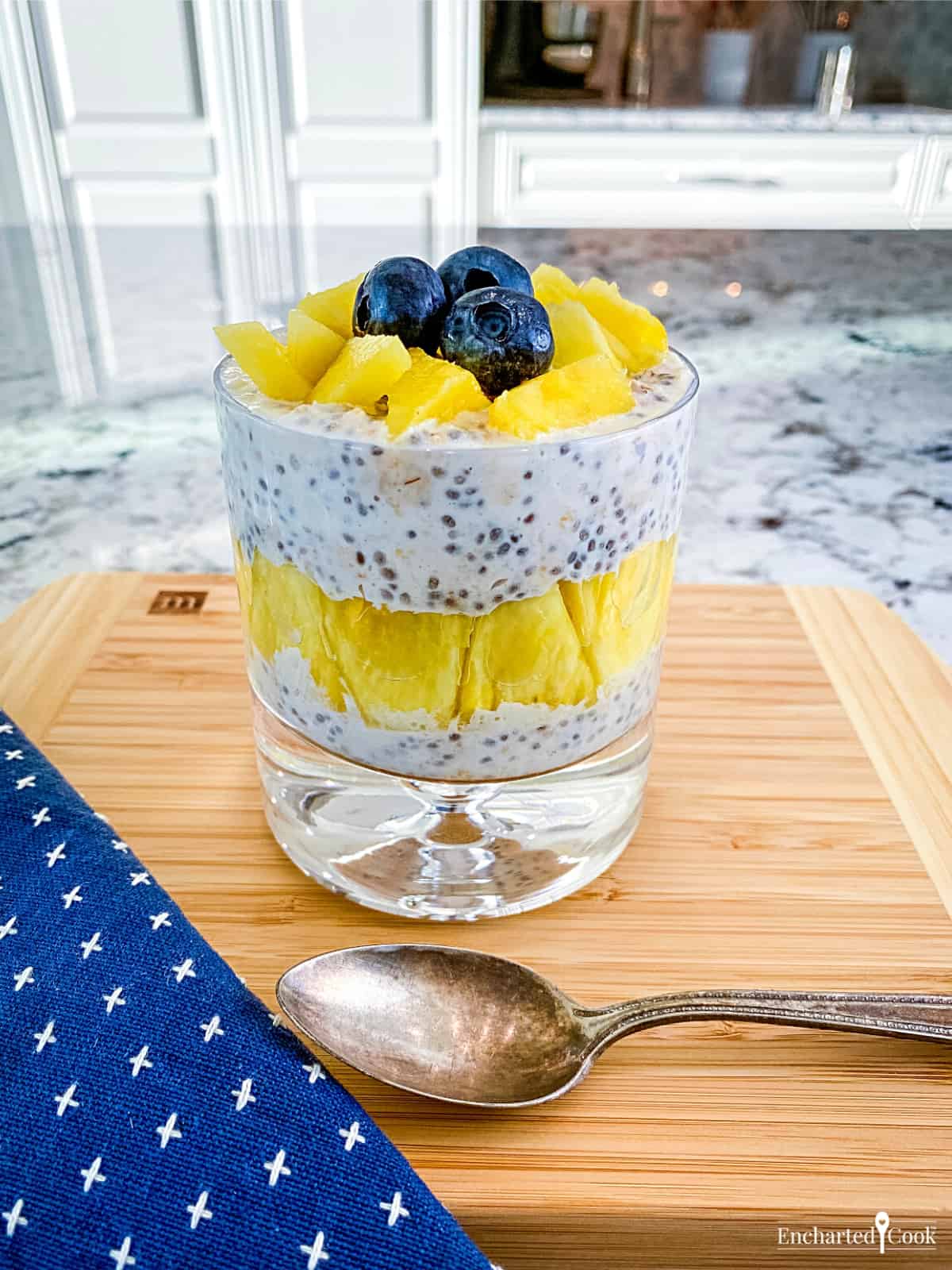 A glass filled with a parfait of overnight oats and fresh pineapple and blueberries.