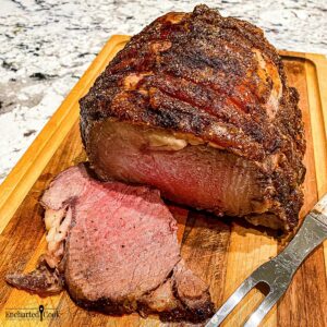A medium-rare standing rib roast being carved on a wooden carving board.