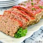 Meatloaf sliced on a white plate is garnished with parsley.