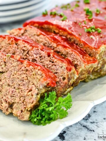 Meatloaf sliced on a white plate is garnished with parsley.