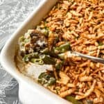 A spoonful of the green bean casserole being lifted from a white baking dish.