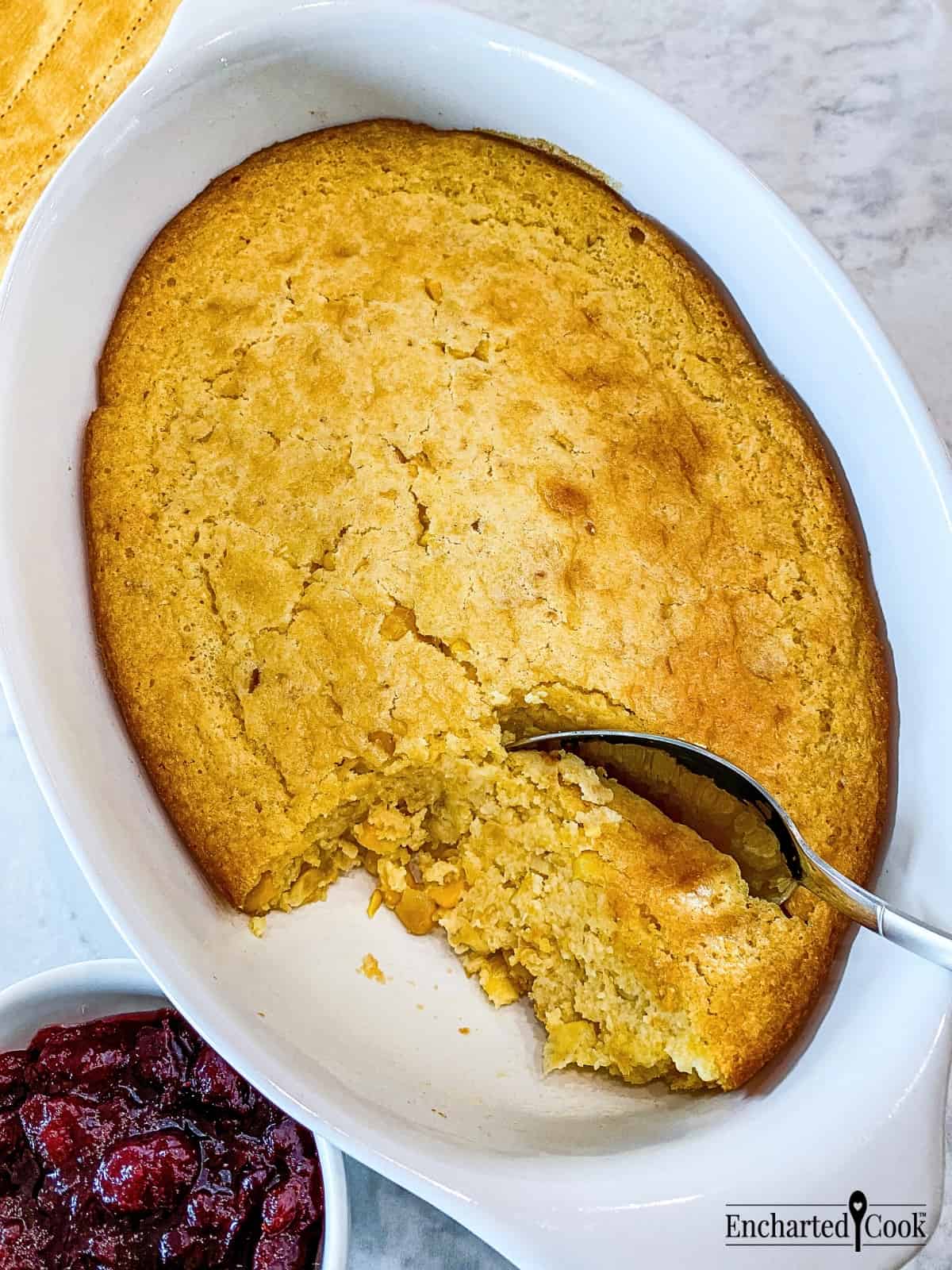 Cornbread casserole baked and ready to be served with a spoon in a white casserole dish.