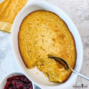 Cornbread casserole baked and ready to be served with a spoon in a white casserole dish.