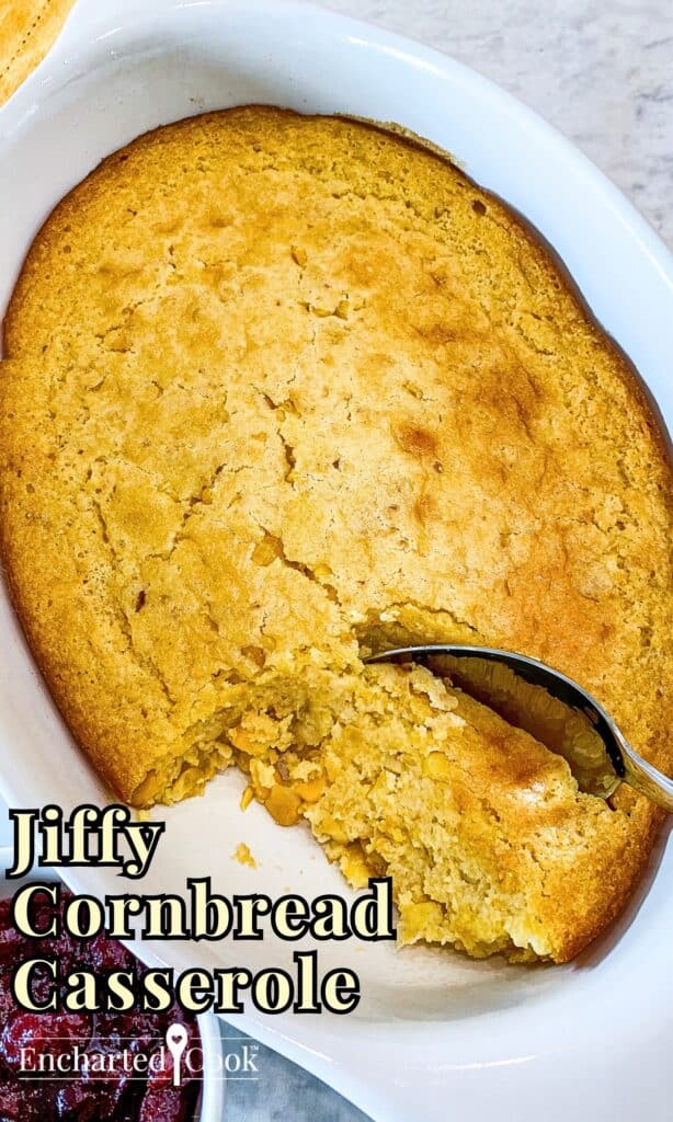 Cornbread casserole baked and ready to be served with a spoon in a white casserole dish with text overlay.