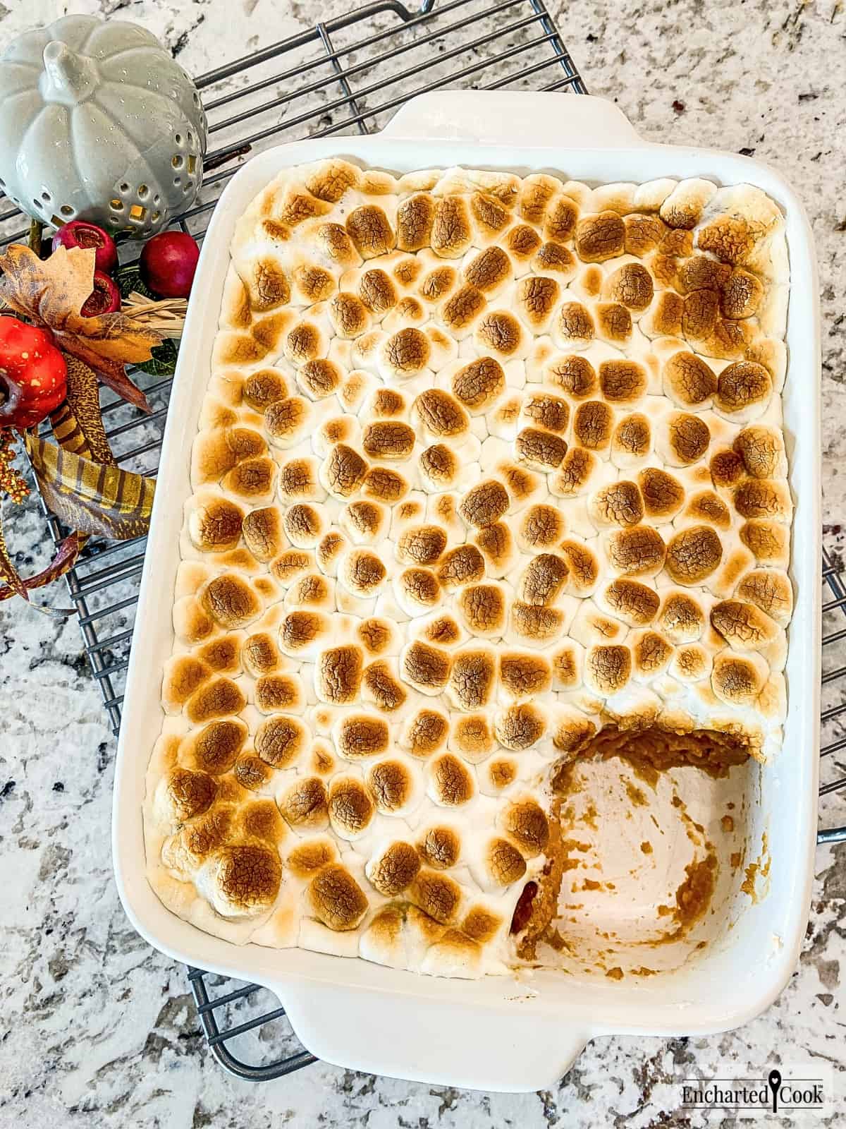 A fully baked sweet potato casserole topped with a layer of melted and toasted miniature marshmallows with a spoonful already served.