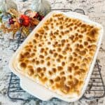 A fully baked sweet potato casserole with a layer of melted and toasted miniature marshmallows on top is ready to be served and enjoyed.