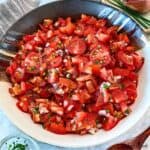 Chopped cherry tomatoes are tossed with chopped shallots, chives, and vinaigrette in a decorative bowl.
