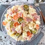 A bowl of potato salad with onions, ham, carrots, and sweet pickles.