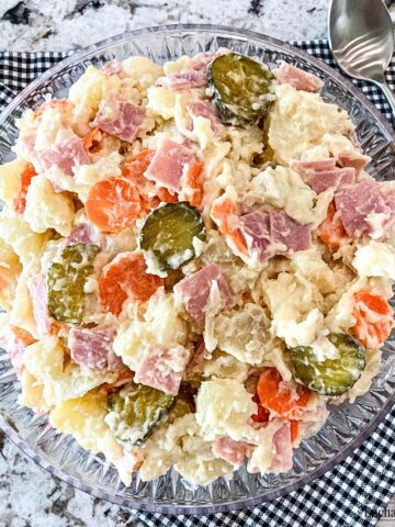 A bowl of potato salad with onions, ham, carrots, and sweet pickles.