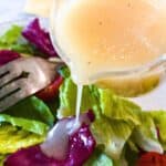 Mustard vinaigrette being poured from a small pitcher onto fresh salad greens.