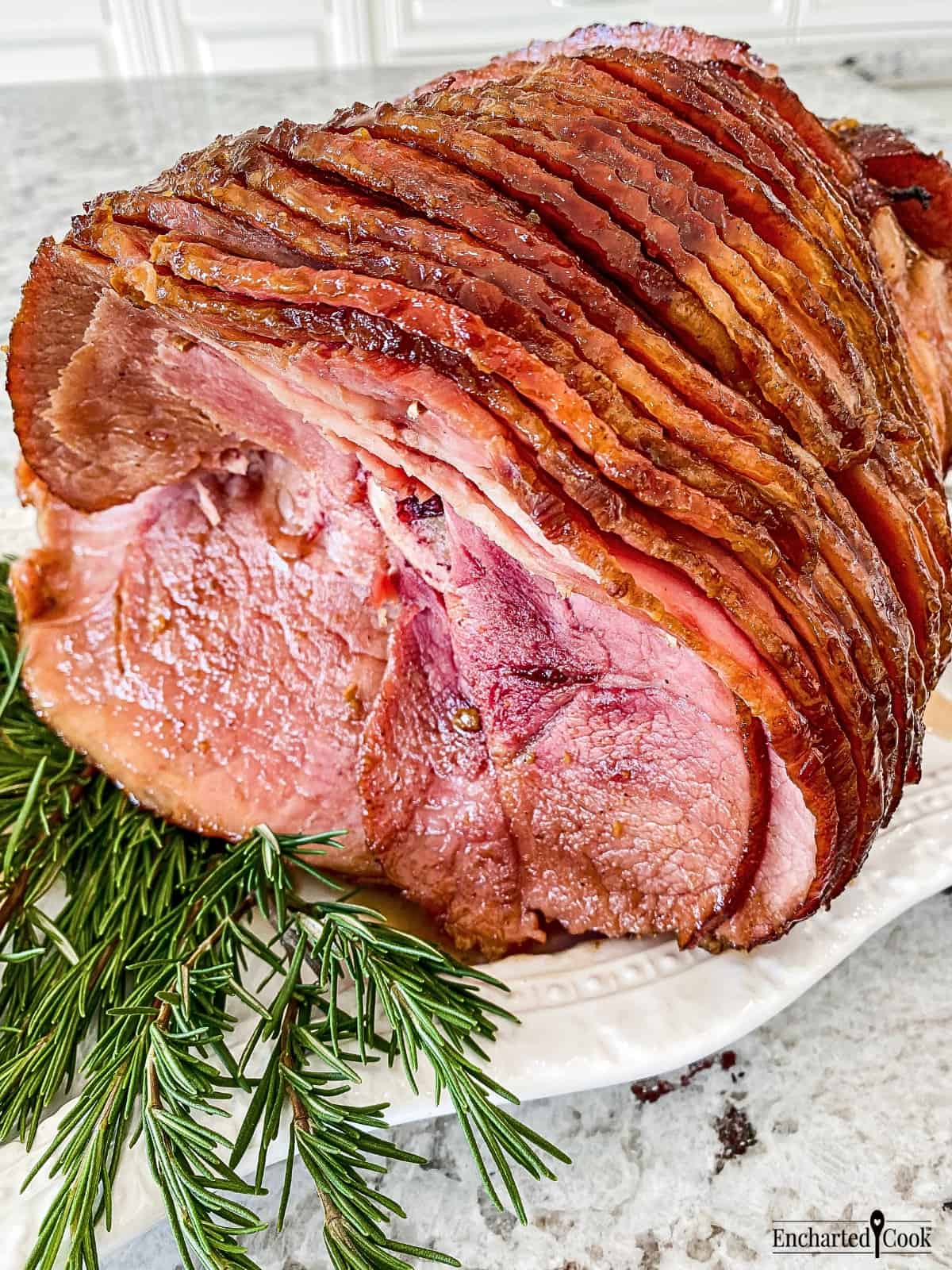 A glazed spiral ham on a white platter with sprigs of rosemary.