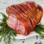 A glazed spiral ham on a white platter with sprigs of rosemary.