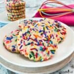 Sugar cookies covered in sprinkles on a white plate.