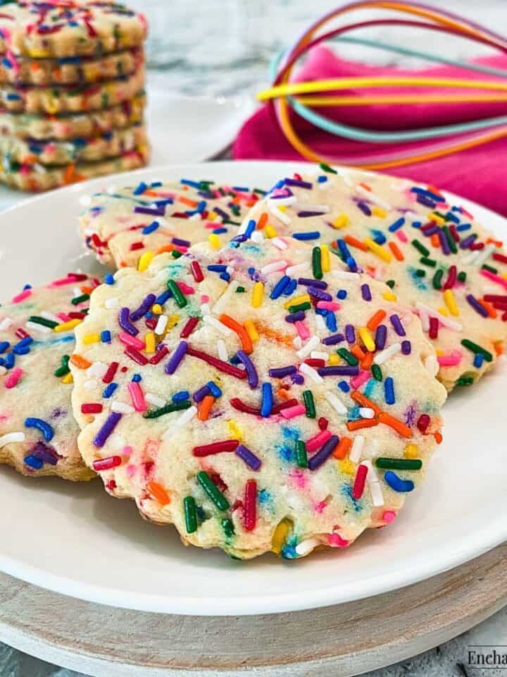 Sugar cookies covered in sprinkles on a white plate.