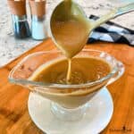 Brown gravy being ladled into a gravy boat.