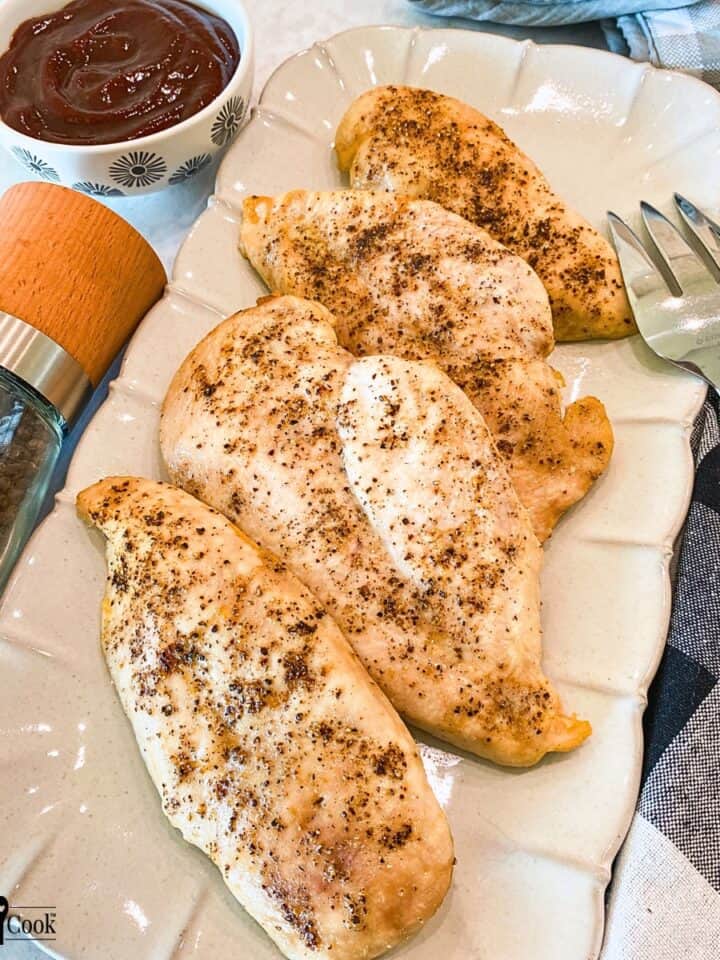 Baked chicken breast with salt and pepper on a beige platter.