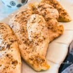 Close up view of baked chicken breast with salt and pepper on a beige platter.