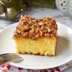 A slice of yellow cake with a broiled caramel and nut topping on a white plate.