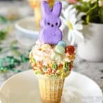 A peeps bunny and jelly beans decorate the top of a decorated cake cone filled with orange fluff.