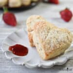 Two heart shaped scones on a beige plate with strawberry jam.