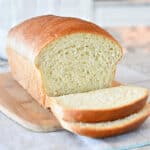 White Sandwich Bread on a wooden cutting board with three slices cut from the loaf.