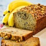 A sliced loaf of banana bread with bananas in the background.