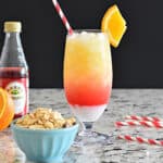Layered cocktail in a tall glass with a red striped straw.