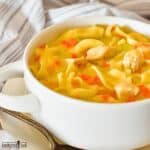 Creamy Chicken Noodle Soup in a white bowl with handles on a plate with a spoon.