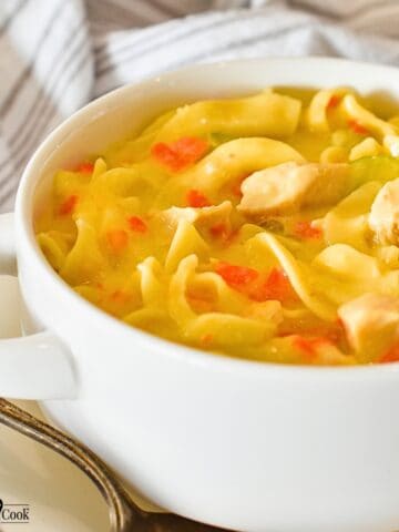 Creamy Chicken Noodle Soup in a white bowl with handles on a plate with a spoon.