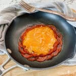 A small non-stick skillet with pepperoni, topped with pizza sauce, and melted cheese.