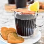 Mulled Red Wine in a clear glass mug garnished with a slice of orange and a cinnamon stick.