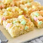 Rice Krispie Treats with pastel mini marshmallows are on a beige cutting board.