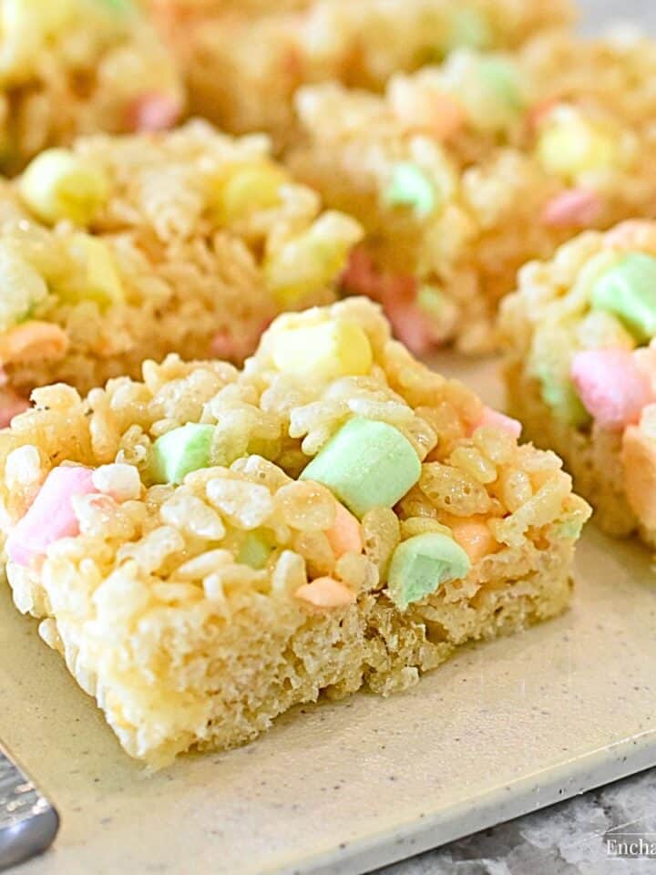 Rice Krispie Treats with pastel mini marshmallows are on a beige cutting board.