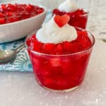 Small glass cup filled with strawberry jello watermelon fruit salad topped with whipped topping.