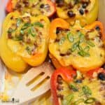 Halved bell peppers stuffed with taco meat, vegetables, and cheese in a white baking dish.