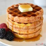 Four chaffles stacked on a white plate with butter, syrup, and berries.
