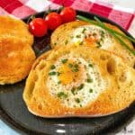 Two Eggs in a Basket are plated with the golden round hole cut-outs with a sprinkling of chopped chives and a few cherry tomatoes.