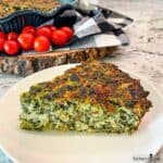 A slice of Spinach and Bacon Crustless Quiche fresh from the oven on a white plate.