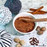 Pumpkin Spice Blend in a small bowl surrounded by cinnamon sticks, whole nutmeg, whole cloves, and dried ginger.