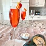 Champagne was slowly poured into the glass and the cocktail is garnished with an orange peel twist and a cherry.