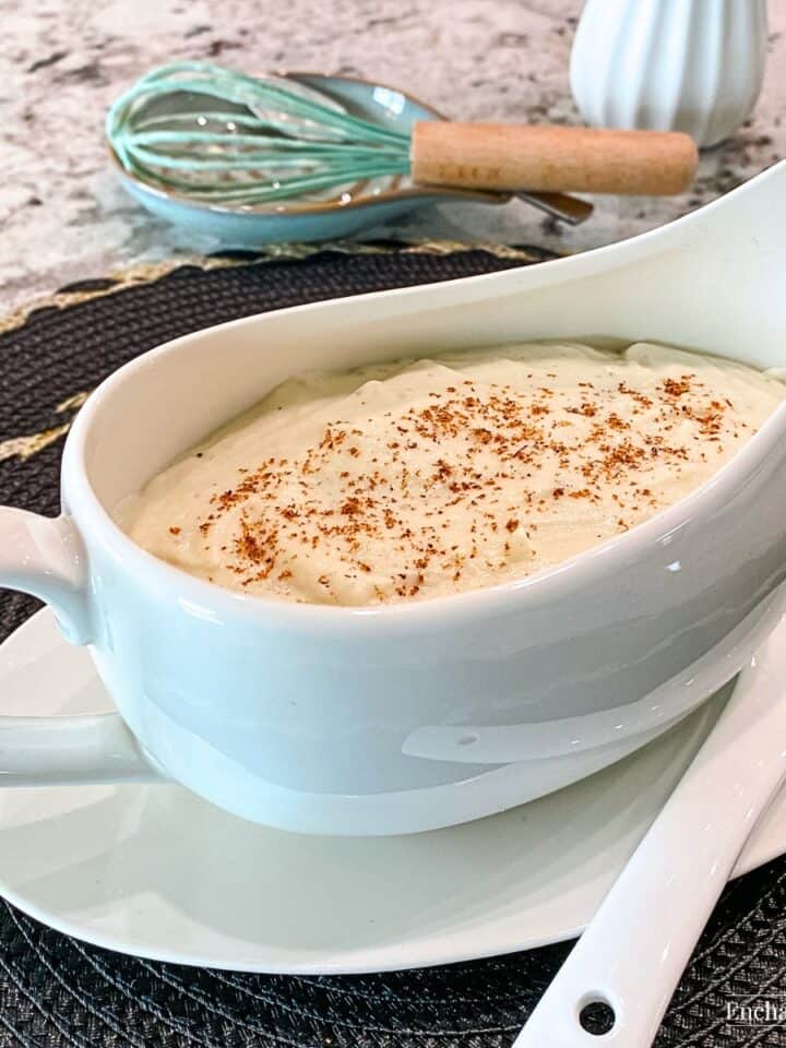 Béchamel Sauce in a white gravy boat garnished with a sprinkling of ground nutmeg.