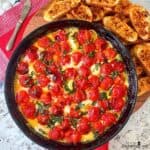Burst Tomato and Mozzarella Spread in a round, black baking dish surrounded by golden toasted crostini.