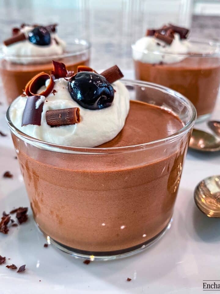 Chocolate Mousse in glass cups topped with whipped cream, chocolate shavings, and a cocktail cherry.