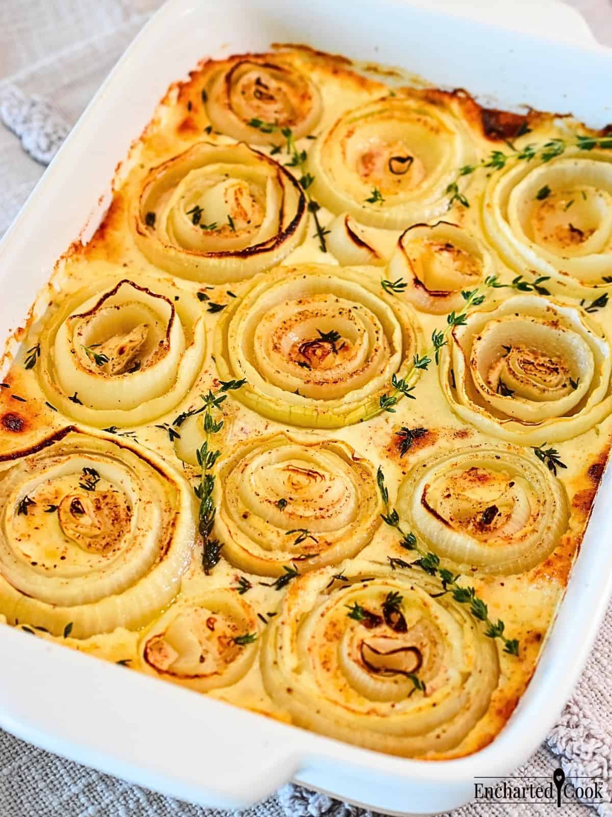 Scalloped onions in a white baking dish and garnished with fresh thyme.
