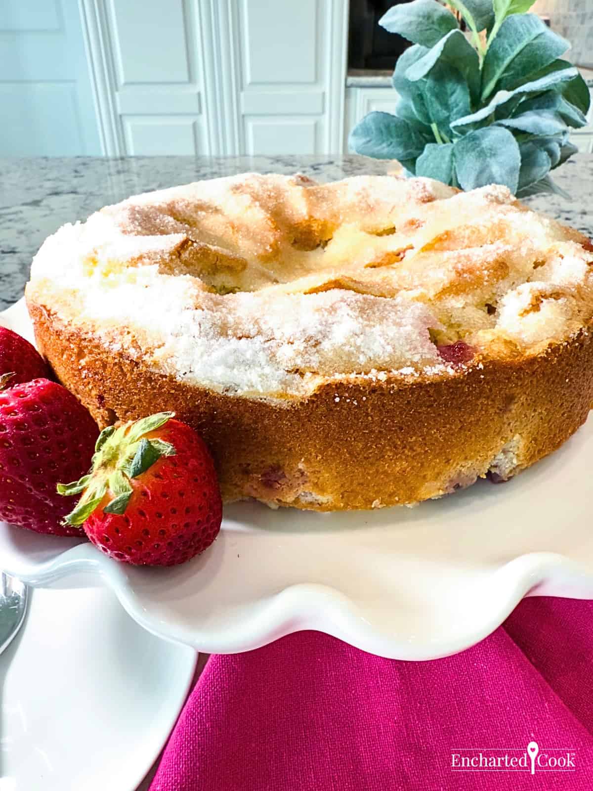 Strawberry French Butter Cake on a white fluted plate garnished with whole strawberries.