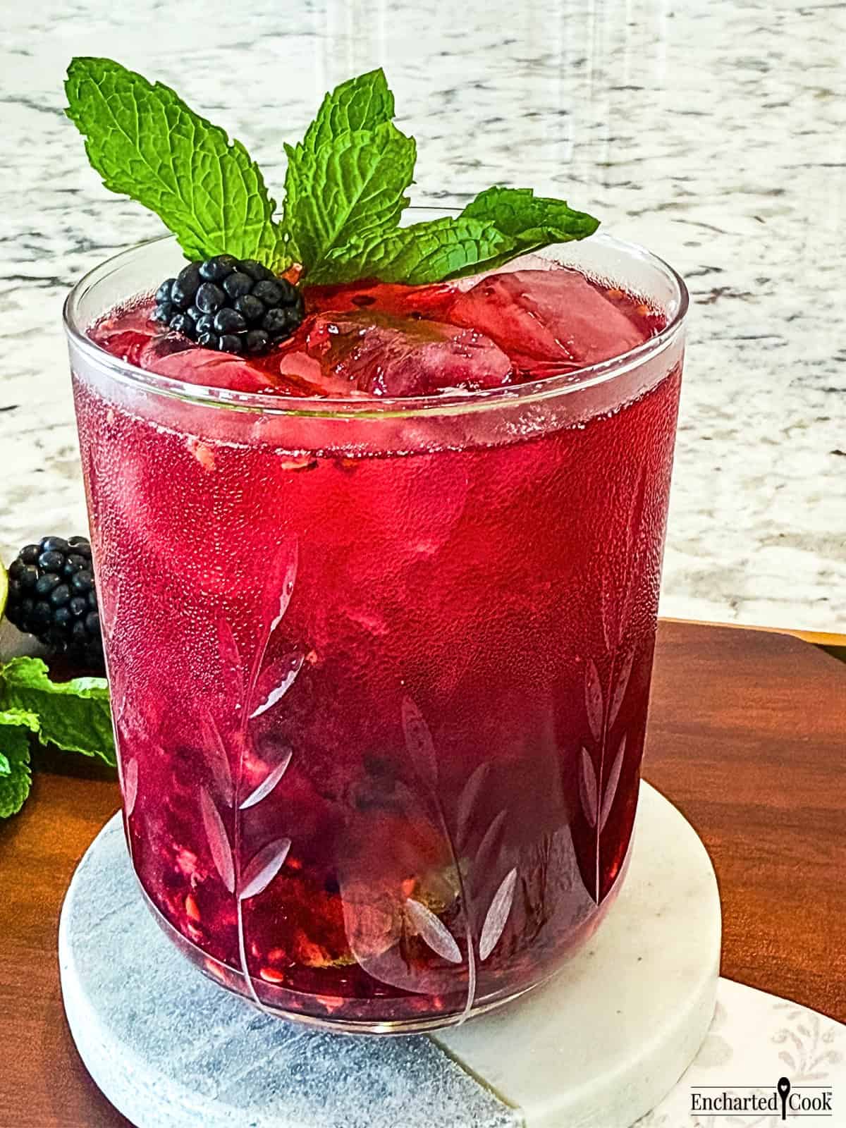 A glass of blackberry cocktail with mint leaves.